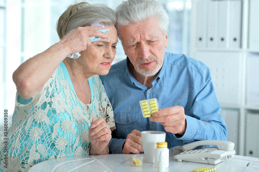 Portrait of ill senior couple with pills posing at home