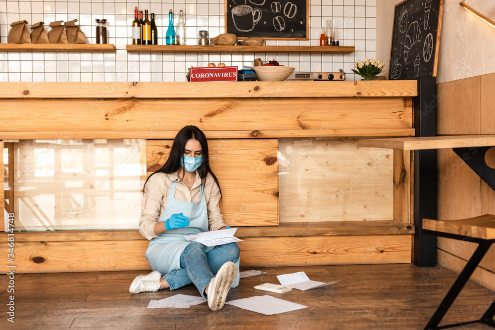 Cafe owner in medical mask reading documents near table on floor Cafe owner in medical mask reading documents near table on floor