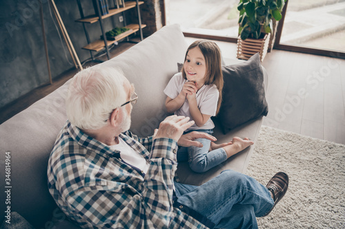 Photo of funny two people old grandpa little interested granddaughter sitting sofa telling good story stay house quarantine safety modern design interior living room indoors