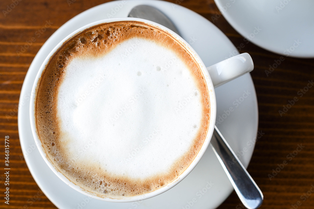 Simple coffee cup with milk foam on a white ceramic plate, on wooden background. Simple coffee cup with milk foam on a white ceramic plate, on wooden background.
