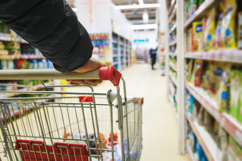 A man with a basket walks in a supermarket. Hand and part of the basket in focus, blurred background
