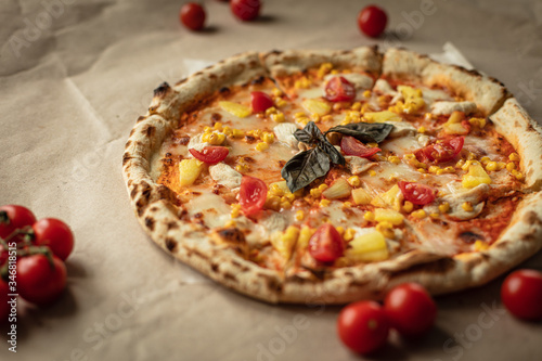 The pizza is big and round on the Kraft paper and wooden tray. Around the tomatoes and top view. The warm tones.