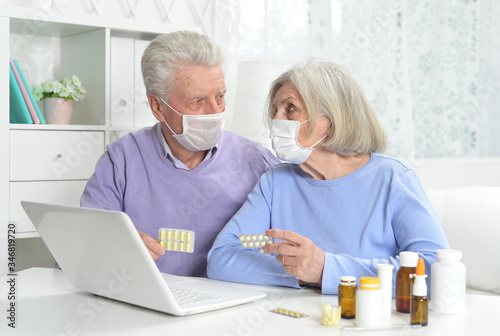 Ill senior couple with facial masks using laptop