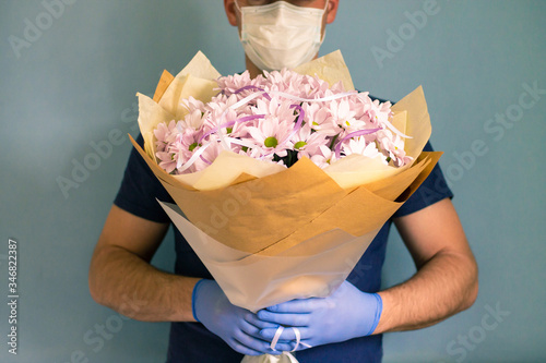 courier in medical gloves and a mask delivers a bouquet of chrysanthemums. Contactless flower delivery during quarantine due to the coronavirus epidemic. photo