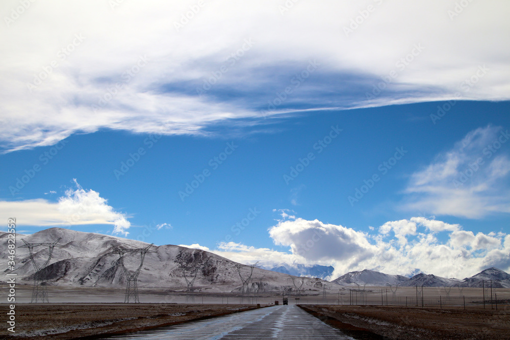 The sky is clear after snow, the snowy mountains in the distance, the blue sky and white clouds, the road to the distance, the high-voltage power transmission line, and the very shocking scenery