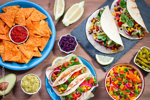Table with tacos, mango salsa, nachos with sauce, guacamole, lemon beer. Appetizers and traditional mexican dishes for cinco de mayo or taco tuesday on wooden table top, copy space photo
