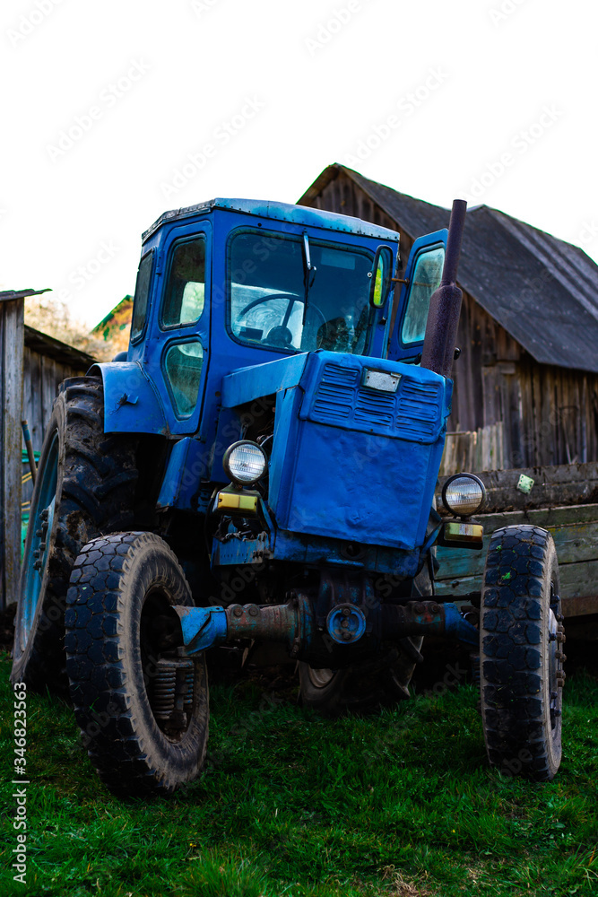 Old vintage blue rusty tractor on the background of farm buildings. Sowing work in the field.