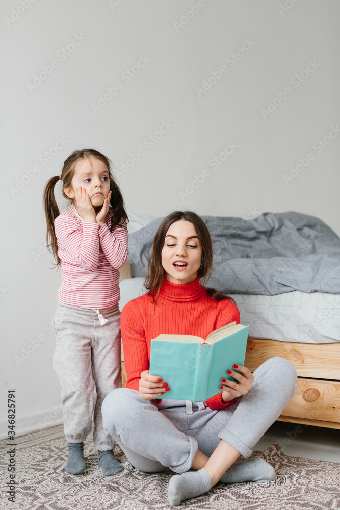 Happy family mother and child daughter reading holding book lying in bed, smiling mom baby sitter telling funny fairy tale to cute preschool kid girl having fun laughing together with bedtime stories