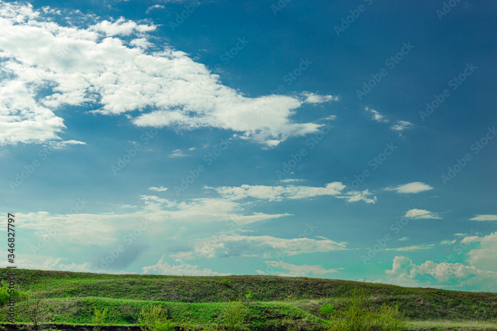 Blue sky with heap white-gray clouds. Horizon green field