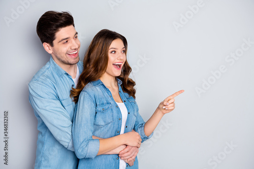 Dear look shopping discounts. Portrait of excited positive couple man hug woman point index finger direct ads promotion wear denim jeans shirt isolated over gray color background