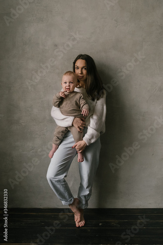 Young beautiful mother plays with her toddler boy son in a living room on the couch. Stylish minimalistic interior, family at home, tenderness, motherhood. © alex