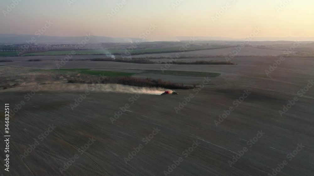 Aerial video flying over red tractor with seeder plows and plants grain seeds in ground of agricultural field. Spring work of fertilized soil preparation on farmland. Drone 4k UHD footage Aerial video flying over red tractor with seeder plows and plants grain seeds in ground of agricultural field. Spring work of fertilized soil preparation on farmland. Drone 4k UHD footage