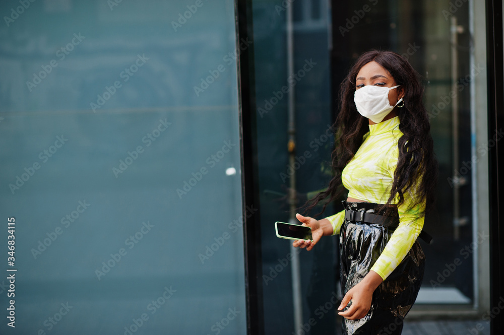 Naklejka premium African American woman posing with facial mask to protect from infections from bacteria, viruses and epidemics and hold mobile phone.
