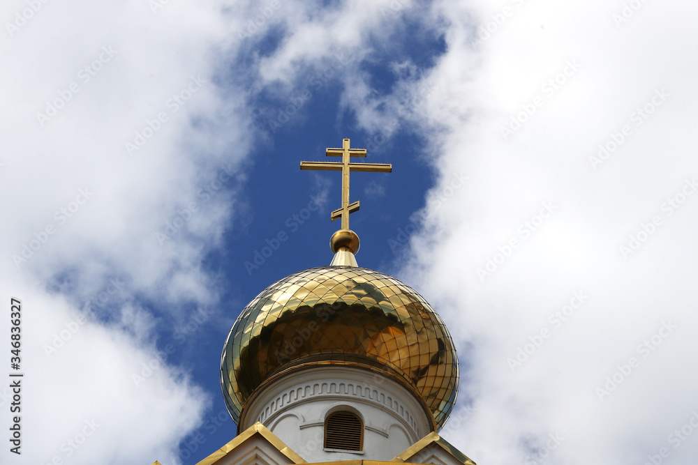 Close-up of the Orthodox golden cross on the roof of the Church against the background of blue sky and clouds