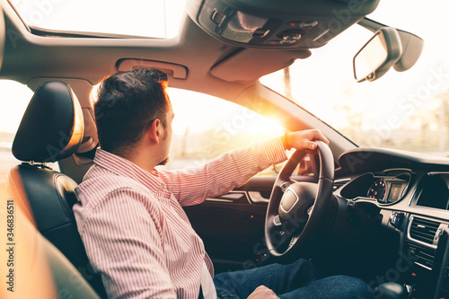 Side view of a driver sitting in comfortable new car with sunroof and looking out the window on sunset