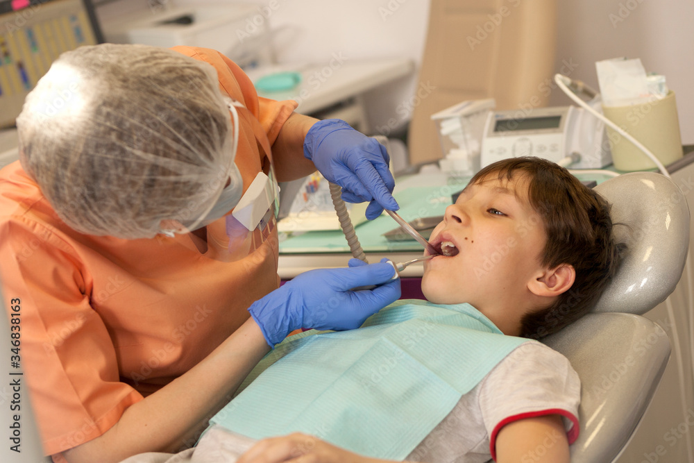 at dentist's appointment. dentist treats boy's teeth with dental tools and saliva pump in the young man's mouth at dentist's appointment. dentist treats boy's teeth with dental tools and saliva pump in the young man's mouth