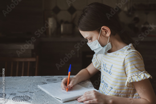 A girl in a protective mask draws with a pen in a sketchbook. Idea for quarantining a child