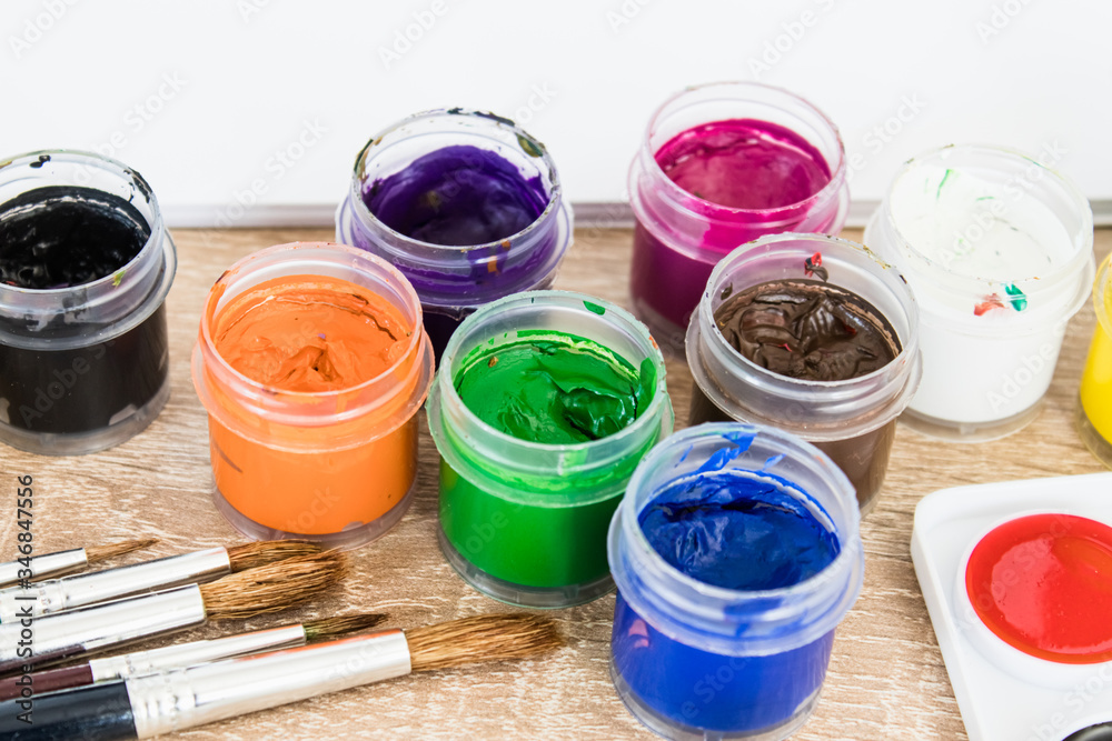 On the table are multi-colored gouache in a jar and brushes for painting. Set for drawing, creativity and hobbies. On the table are multi-colored gouache in a jar and brushes for painting. Set for drawing, creativity and hobbies.