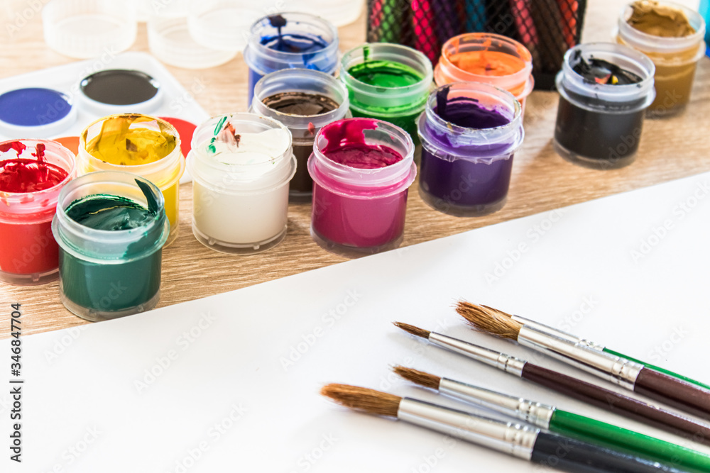 On the table are multi-colored gouache in a jar and brushes for painting. Set for drawing, creativity and hobbies. On the table are multi-colored gouache in a jar and brushes for painting. Set for drawing, creativity and hobbies.