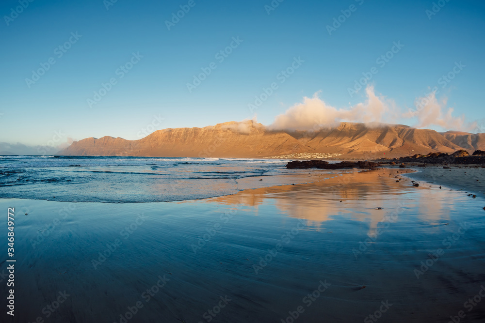 Fototapeta premium Famara beach with reflection and mountains at sunset in Lanzarote at Canary islands