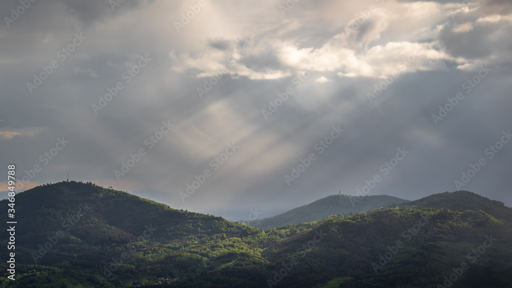The sun shines thru the clouds during a rain shower over ther Merkur and Fremersberg Mountain near Baden-Baden Germany The sun shines thru the clouds during a rain shower over ther Merkur and Fremersberg Mountain near Baden-Baden Germany