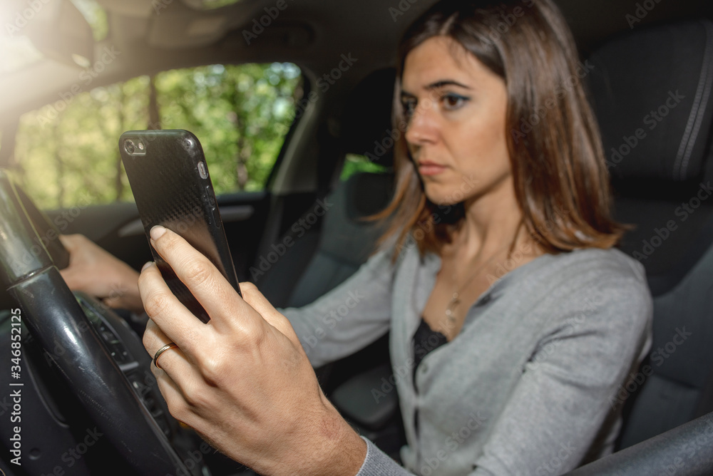 Portrait of young woman driving car while texting on the mobile phone risking to cause a traffic accident. Driving offense.