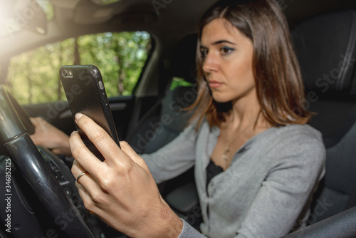Portrait of young woman driving car while texting on the mobile phone risking to cause a traffic accident. Driving offense. © Pintau Studio