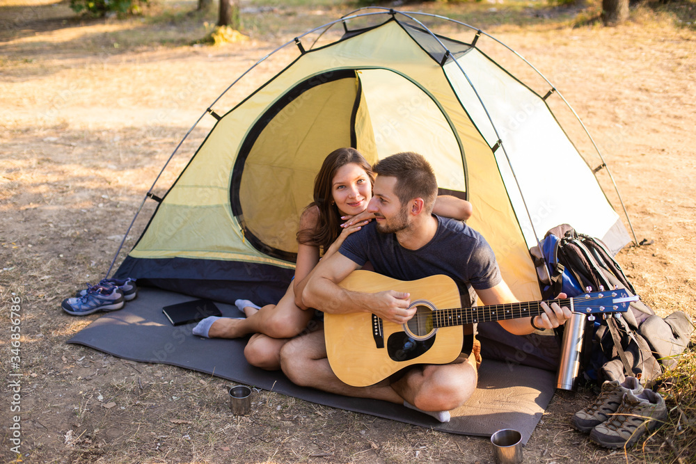 A man plays for a woman on a guitar near a tent at sunset. Honeymoon in the hike