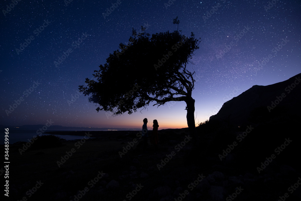 Silhouette of couple with night scene milky way background in the galaxy. under tree. Romantic star night shot
