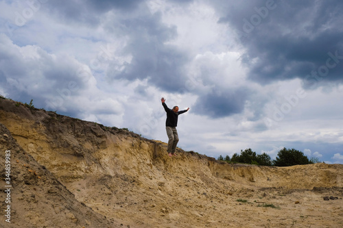 Sand quarry and silhouette of a sporty man jumping down on a background of rain clouds. Ukraine. 