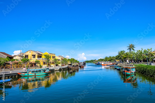 Hoi An ancient town in the sunshine day with blue sky, fishing boats, ancient houses reflect on the river. Hoi An is a popular tourist destination in Quang Nam, Vietnam. Landscape photography. © Shinigamj