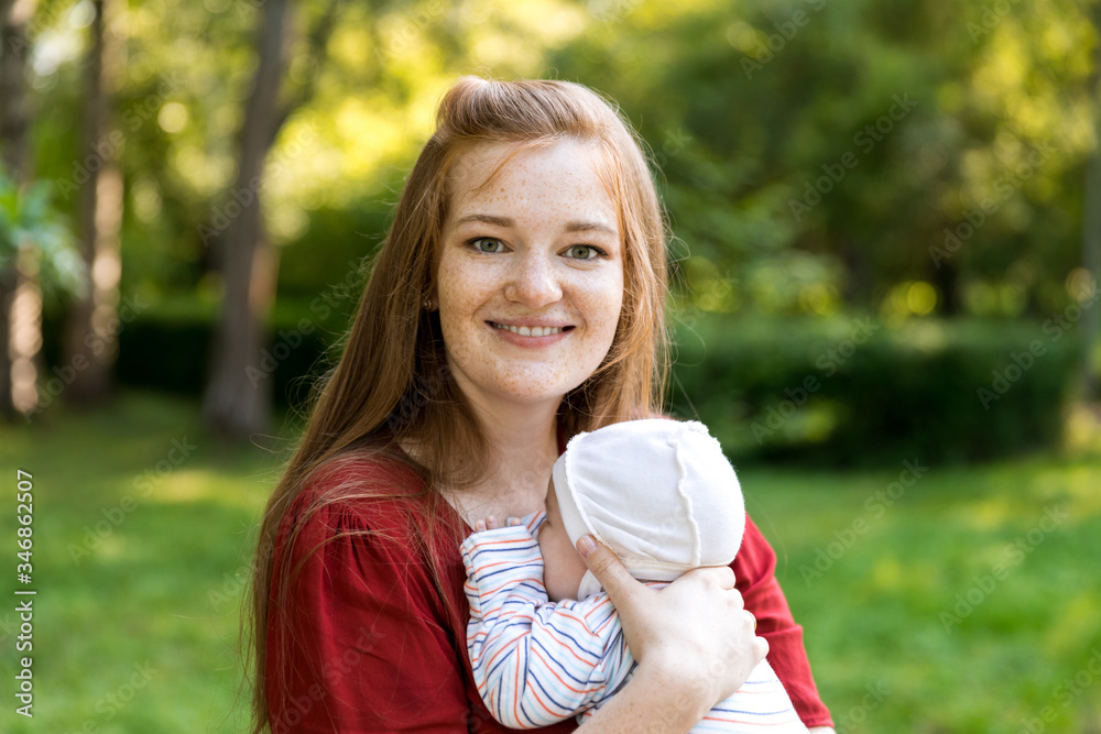 Young mother gently applied to her chest her two-month-old newborn baby in the summer green park. Moments of happy motherhood