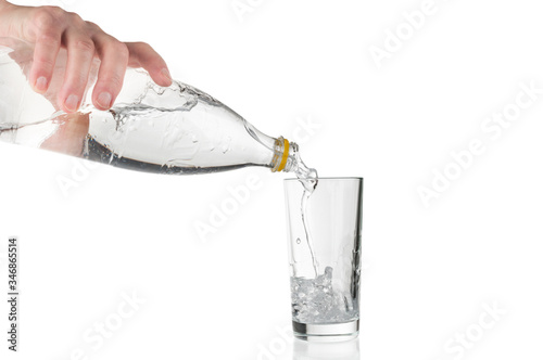 Hand pouring soda water from plastic bottle into glass on white background