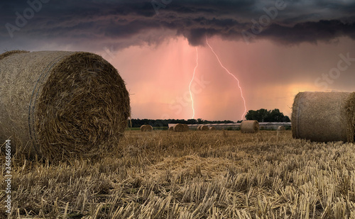 Slika na platnu Summer thunderstorm and lightning and looms over harvested hay field with hay ba