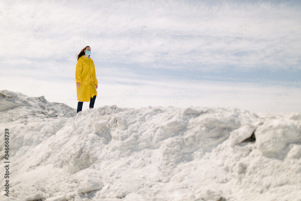 Young woman walking on a phosphate mountain that was made by chemical plant waste. She is wearing yellow protective coat and a mask. Ecology protection awareness