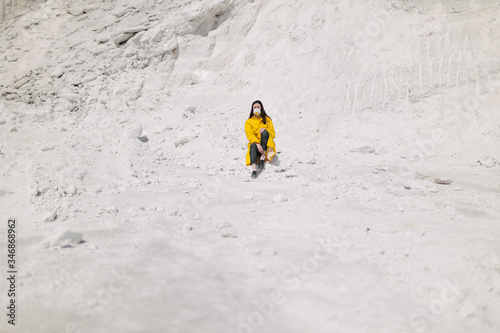 Young woman walking on a phosphate mountain that was made by chemical plant waste. She is wearing yellow protective coat and a mask. Ecology protection awareness
