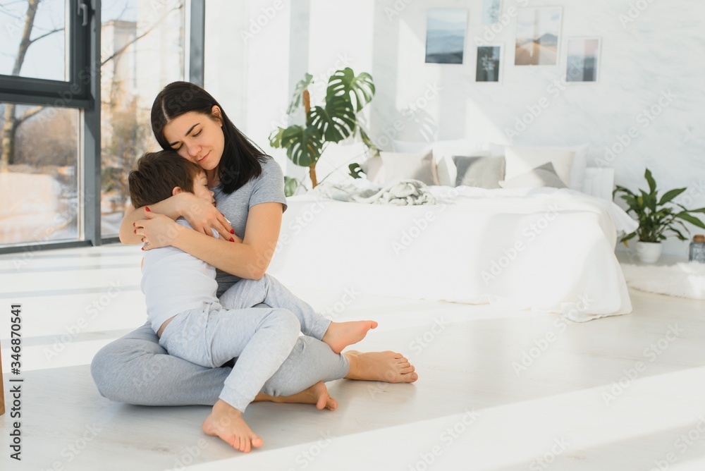 Cheerful mother sitting on couch in cozy light living room holds on lap tickles of little son enjoy funny activities on weekend at home, have fun together, priceless time with preschool child concept Cheerful mother sitting on couch in cozy light living room holds on lap tickles of little son enjoy funny activities on weekend at home, have fun together, priceless time with preschool child concept