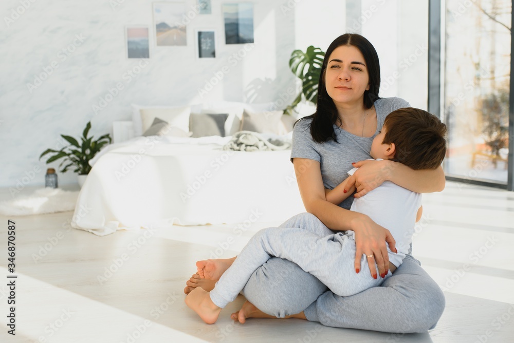 Cheerful mother sitting on couch in cozy light living room holds on lap tickles of little son enjoy funny activities on weekend at home, have fun together, priceless time with preschool child concept Cheerful mother sitting on couch in cozy light living room holds on lap tickles of little son enjoy funny activities on weekend at home, have fun together, priceless time with preschool child concept