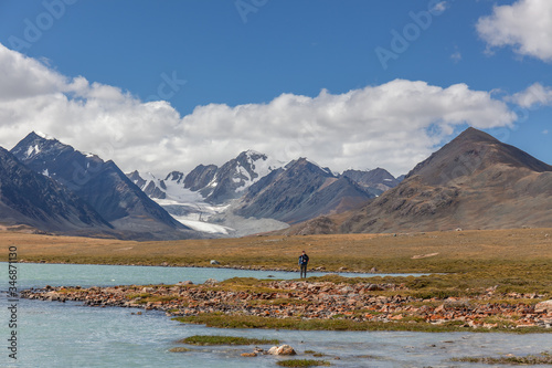 A tourist walks along the grass near the mountain lake of the Mongolian Altai
