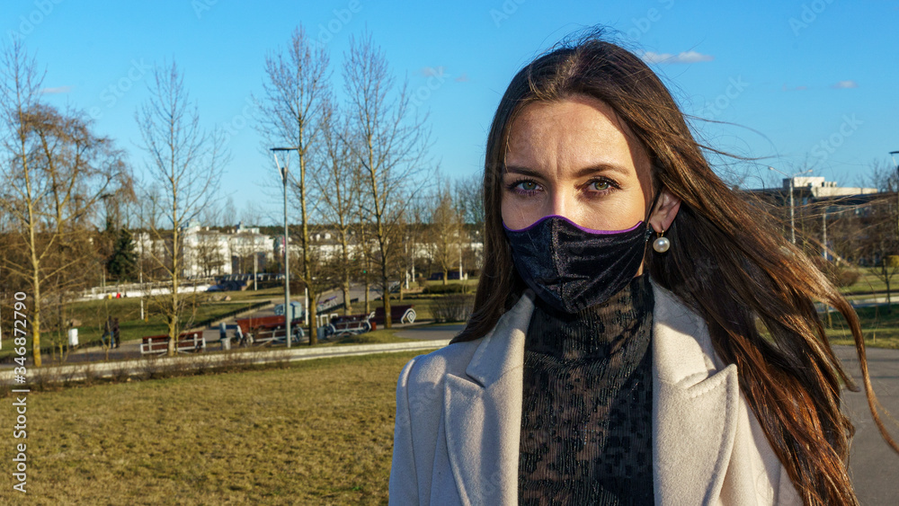 Coronavirus fashionable medical face mask worn by young female with dark long hair, standing at tram stop on a urban city street on dusk. Stop covid 19 pandemic or air pollution concept. Coronavirus fashionable medical face mask worn by young female with dark long hair, standing at tram stop on a urban city street on dusk. Stop covid 19 pandemic or air pollution concept.