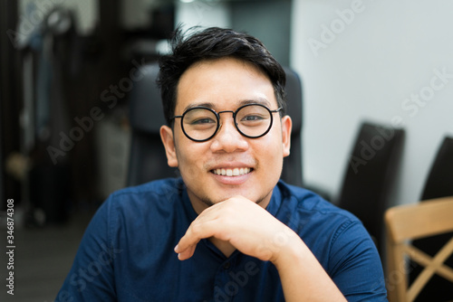 A young asian man, around 30 years old, good looking, wearing glasses, wearing a blue shirt Sit and work at home photo