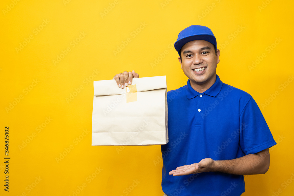Blue Delivery handsome asian man holding paper bag on isolated yellow background. Blue Delivery handsome asian man holding paper bag on isolated yellow background.