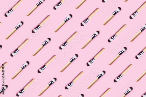 Pattern made from make up brushes on pink background.