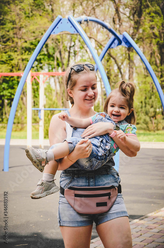 May 2020. Kiev Ukraine. A little girl plays outside in a park, collects plants on a sunny day in denim overalls and a T-shirt with a print  LOL
