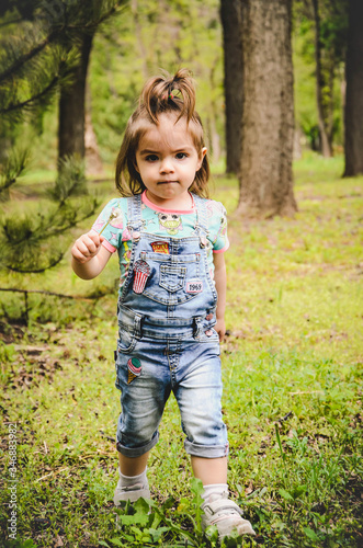 May 2020. Kiev Ukraine. A little girl plays outside in a park, collects plants on a sunny day in denim overalls and a T-shirt with a print LOL