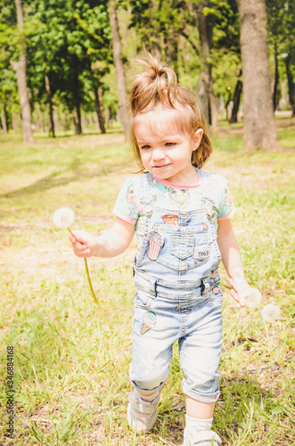 May 2020. Kiev Ukraine. A little girl plays outside in a park, collects plants on a sunny day in denim overalls and a T-shirt with a print  LOL