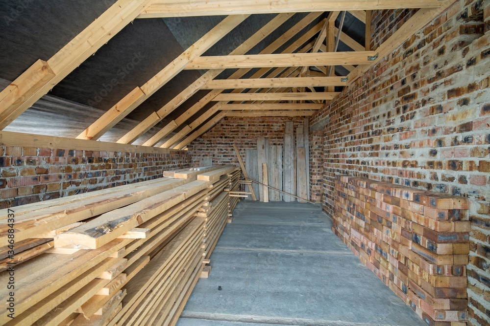 Fototapeta premium Interior of unfinished brick house with concrete floor, bare walls ready for plastering and wooden roofing frame attic under construction.