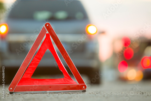 Red emergency triangle stop sign and broken car on a city street.