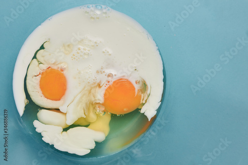 eggs and milk are mixed in a glass cup on a blue background. top view