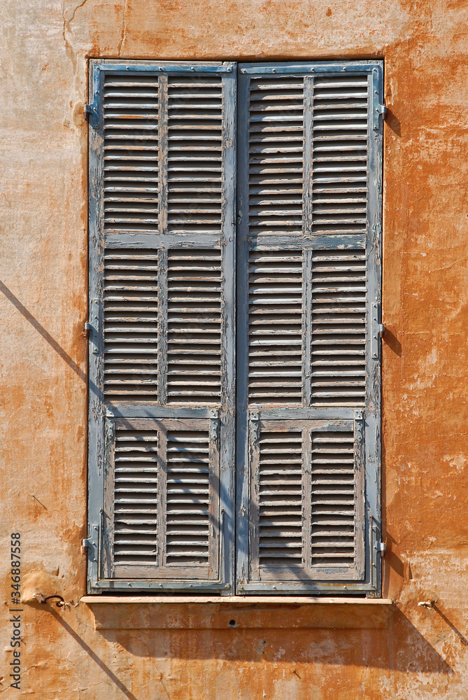 Alter, hellblauer hölzerner Fensterladen in orangfarbener Hausfassade